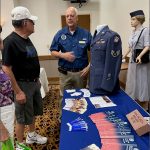 Guests and volunteers discuss uniforms over a table.