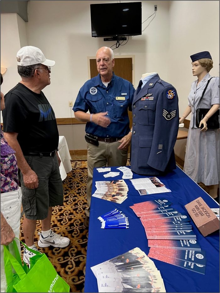Guests and volunteers discuss uniforms over a table.