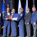 Six individuals stand on stage as award is given.